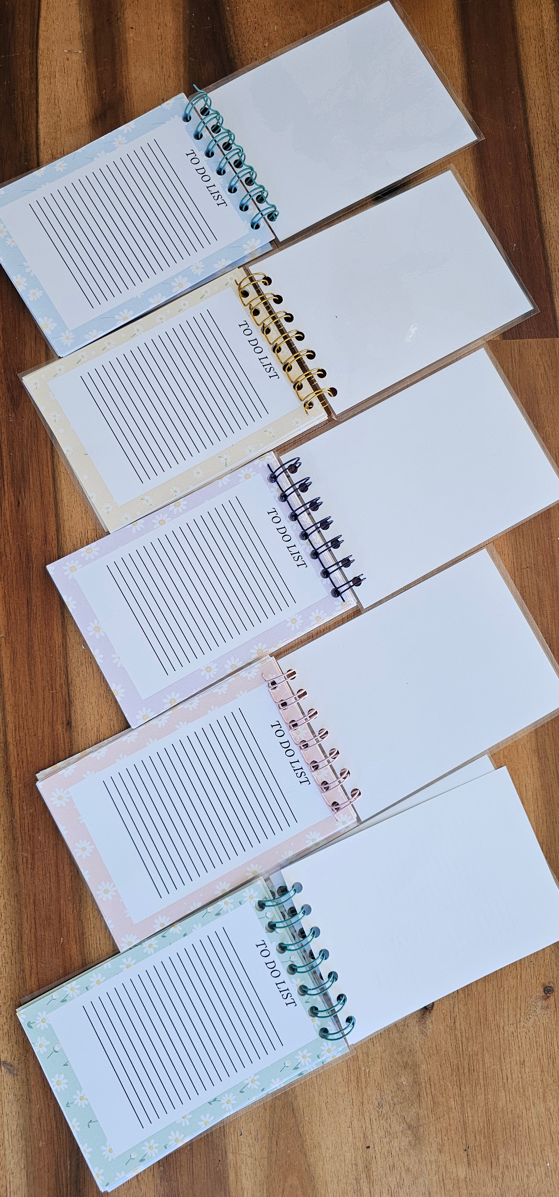 Carnets printaniers ouverts avec pages To Do List, motifs de marguerites pastel faits main, reliure spirale, présentés sur table en bois